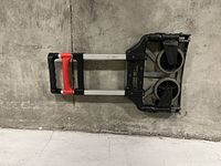 Side view of a folding trolley cart with aluminum frame against a concrete wall