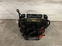 Portable Eliminator branded jump starter with booster cables attached, viewed from above and with handle visible.