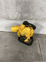 Yellow handheld leaf blower resting on a cement floor against a concrete wall