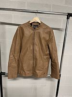 Front view of brown leather jacket showing zipper closure and two side pockets.