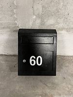 Front view of the black metal mailbox showing white number 60, mail slot, and lockable door.