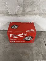 Closed red Milwaukee M18 2630-20 circular saw box labeled tool-only, placed on concrete floor with plain wall background.