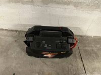 Front view of the black Motomaster Terminator Powerbox showing integrated handle, control panel, and attached red jumper cables.