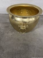 Front and side views of the hammered brass planter with decorative lion head ring handles and wide rim.