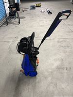 Front angled side view showing blue body, black hose reel with coiled hose, and handle.