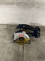 Cordless Ryobi circular saw powered by an 18V battery, placed on concrete floor against a wall.