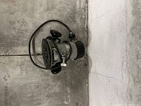 Electric motor assembly with pulley and cord placed on concrete floor against wall.