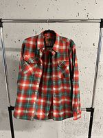 Front view of men's medium plaid button-up shirt on hanger showing front pockets and button details.