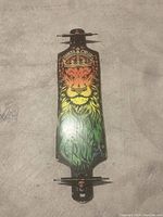 Longboard skateboard featuring a lion head graphic with a crown, painted in red, yellow, and green hues. Trucks and red wheels attached. Deck appears in good condition with minor surface wear.