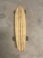 Top view of vintage wooden skateboard showing natural wood grain deck with striped design and four black wheels.
