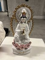 Front view of porcelain Guan Yin statue showing detailed face, pink lotus base, and gold-tone halo flames.