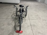 Front view of metal gray adult tricycle showing single front wheel, handlebars and front tire