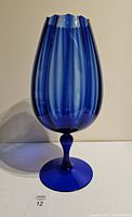 Front view of a deep blue glass pedestal vase with a tulip-shaped, vertically ribbed body and scalloped rim, set against a plain background.