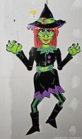 Full view of the large diecut witch decoration showing the entire figure with arms extended, on a plain wall background.