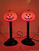 Pair of Halloween candle sticks, one with illuminated smiling jack o lantern pumpkin top, the other a candle stick with flame-shaped bulb, black bases and electric cords