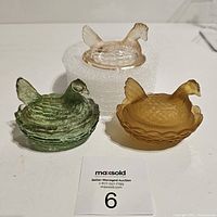 Three miniature hen on nest art glass boxes; one green, one amber, one clear lid only, displayed together.