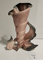 Full side view of the pink shell-shaped vase with fish base, showing the spiraled hollow body and curled opening.