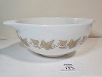 Side view of white Pyrex Cinderella mixing bowl with brown Sandlewood leaf and bird pattern on the exterior, showing spout and handle.