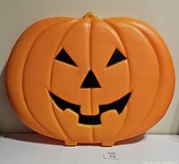 Front view of orange plastic flat blow mold in the shape of a pumpkin with carved face and a tooth in the smile.