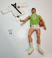 Photo showing Big Jim figure dressed in green basketball jersey number 9, white shorts, socks, sneakers, holding basketball, with white martial arts gi jacket beside him.