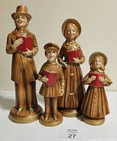 Front view of the four vintage carolling family figurines with neutral brown tones and red books