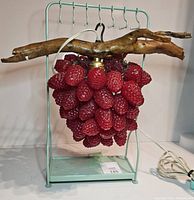 Front view of lamp on mint green metal stand with driftwood branch and red raspberry cluster.