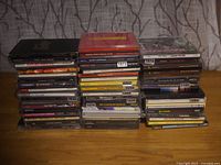 Photo showing a large stack of assorted audio CDs with various artists and titles, stacked on a wooden surface.