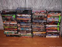 Wide photo showing multiple stacks of DVDs and Blu-ray discs arranged on a wooden surface with visible titles including Batman Forever, Batman & Robin, Batman Returns among others