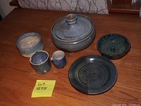 Group of six blue pottery dishes including a large lidded pot, plate, small jug and cup, and two bowls on wooden surface