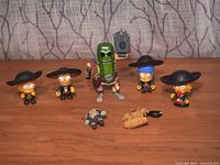 Full view of 4 Mariachi Simpsons figures in black mariachi outfits, Pickle Rick Funko Pop figure holding a bottle, and 2 miscellaneous blind box keychains on wooden surface.
