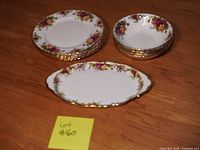 Shows full set of plates, bowls, and serving plate with floral and gold pattern on wooden surface
