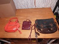Three leather bags on wooden table showing different sizes and colors