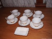 Full set of 6 white teacups and saucers with single matching candy dish on wooden surface