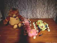 All three plush toys on wooden table, showing Teddy Ruxpin and two caterpillar plushes