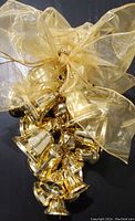 Close-up of the cluster of 24 golden metal bells attached to a large sheer golden ribbon bow, showing the glossy metallic finish and attached strikers.