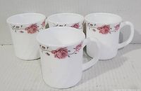 Four white opal glass mugs displayed side by side with pink rose floral pattern near the rim