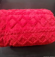 Close-up of folded red plush blanket with diamond textured pattern.