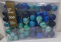 Clear plastic box showing 100 Christmas tree ball ornaments in shades of blue and green with different finishes, unopened and in new condition