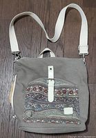 Gray high density canvas backpack with colorful front pocket and white adjustable straps, laid flat on wooden floor.