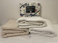 Overview photo showing three folded blankets (two white Ralph Lauren blankets and one cream Ralph Lauren blanket) stacked with a boxed Laura Ashley queen sheet set on top.