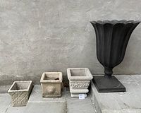 Photo showing arrangement of all four urns together: three small-to-medium sized square cement urns and one large black urn with petal-shaped rim.