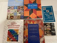 Photo showing all 6 main quilting books with colorful covers and 2 quilting booklets, arranged flat on a white table.