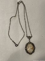 Full view of the cameo necklace showing the chain and pendant with the detailed cameo over a white fabric background.
