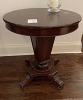 Front view of antique mahogany round pedestal side table showing round top, beaded apron edge, tapered pedestal with vertical grooves, and ornately carved feet.