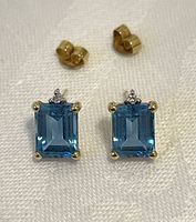 Front view of both stud earrings showing emerald-cut blue topaz and diamond accents