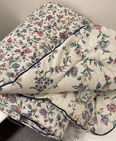 King size comforter folded showing dense multicolor floral pattern with blue piping trim.