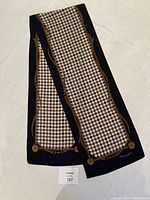 Full length view of folded silk scarf showing central beige, brown, and black checkered pattern and decorative brown belt motif border.