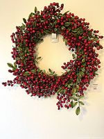 Photo showing vibrant red berry Christmas wreath hanging on a wall. The wreath consists of clusters of red berries and green leaves with an approximate diameter of 16-18 inches.