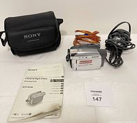 Full set overview of Sony Handycam DCR-HC26 camcorder with accessories including battery pack, charger, carrying case, and operating guide on white surface.