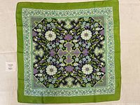 Full view of the square Liberty of London silk scarf laid flat showing the vibrant floral pattern and green border.